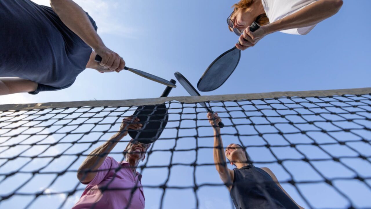 Four pickleball players stand over a new